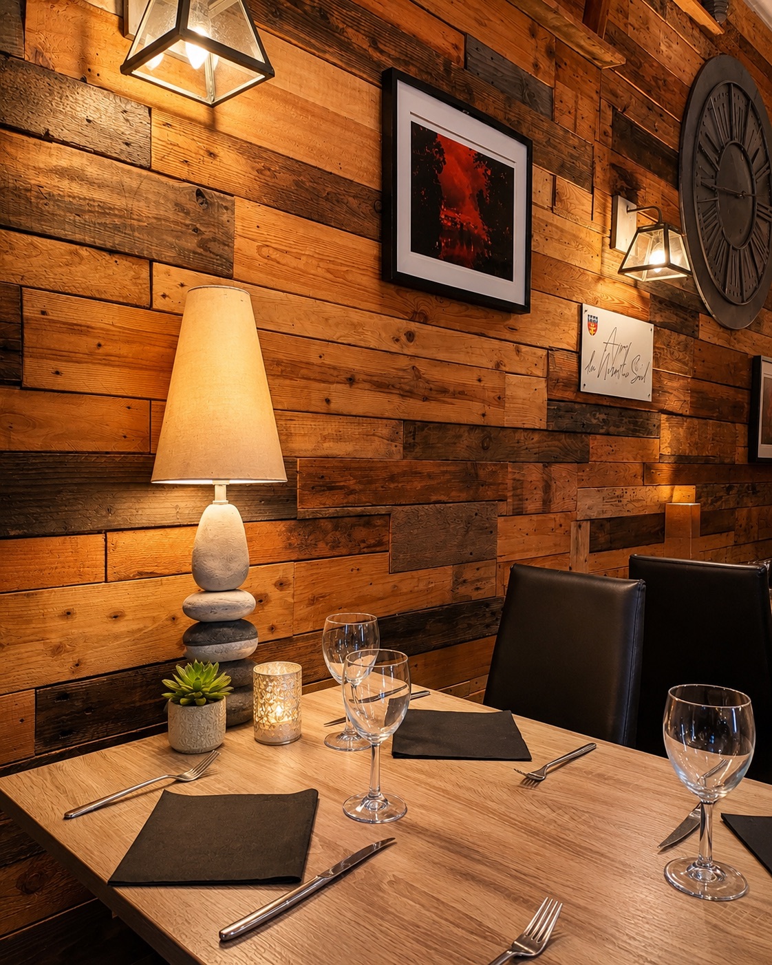 Détail de la salle : mur en bois patiné, lampe allumée, table dressée avec verres et serviettes ardoise